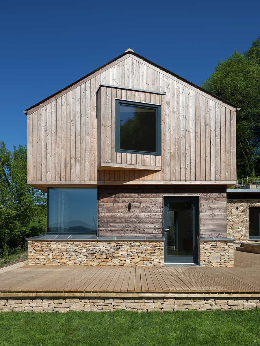 The Larch House front elevation with larch cladding, Cotswold stone plinth and timber deck, daytime